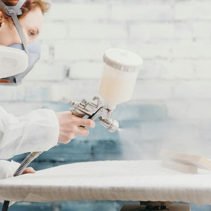 Professional furniture refinisher using spray gun and safety equipment to apply catalyzed lacquer finish to wooden door